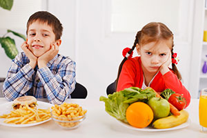 Boy and girl with fast food and vegetables