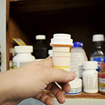 Child reaching for prescription bottle in medicine cabinet.