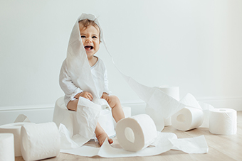 Laughing toddler wrapped in toilet paper sitting on a training potty