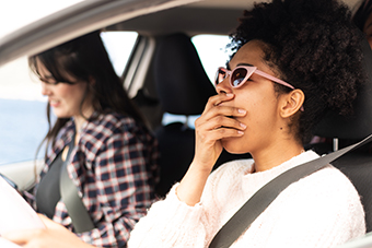 Young adult woman yawning while driving with another young adult woman in the passenger seat