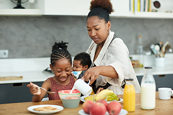 Mom pouring milk in her daughter's cereal