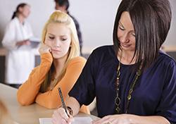 mom filling out paperwork at doctor's office with teen